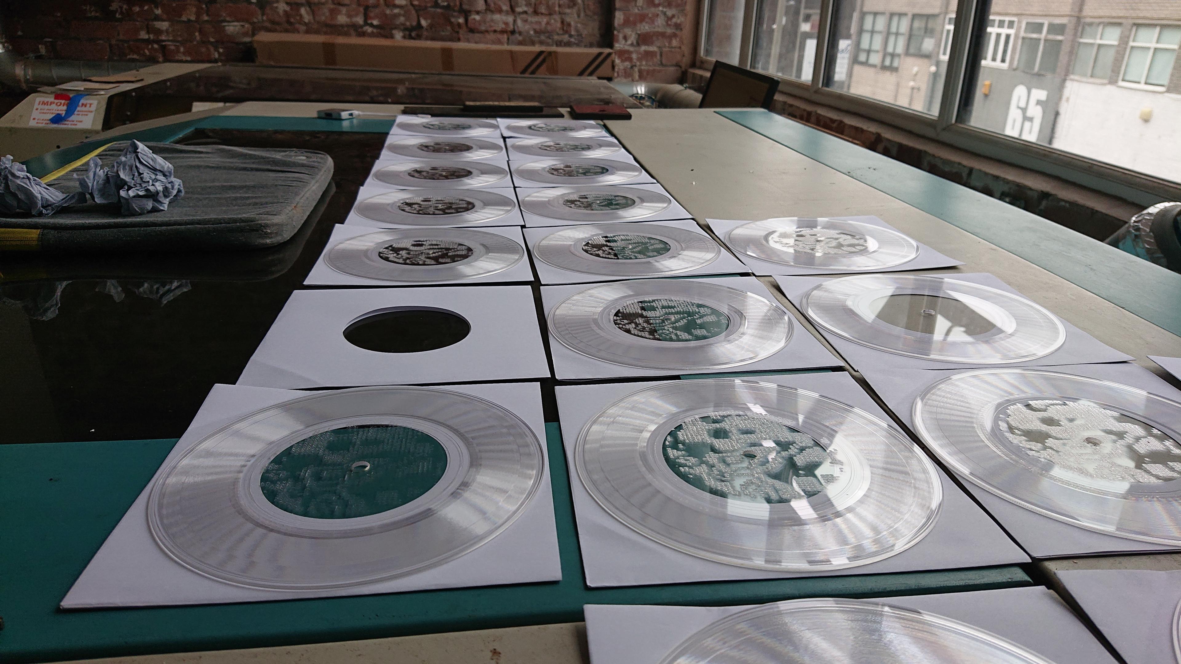 A grid of transparent 7 inch records laid out across the lid of one of the laser cutters in the DoES Liverpool workshop