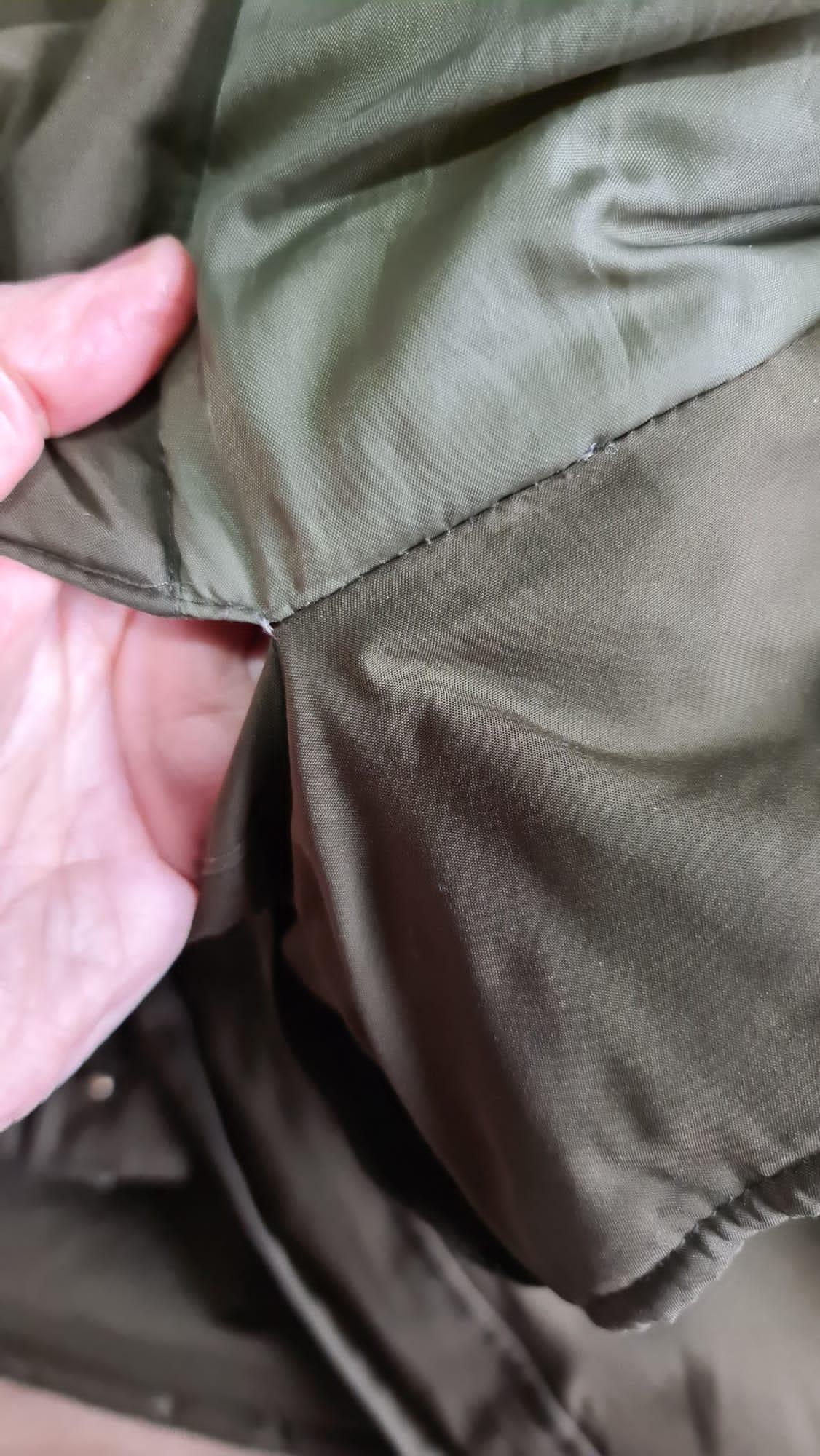 An olive green coat being held open to show a hand-stitched seam