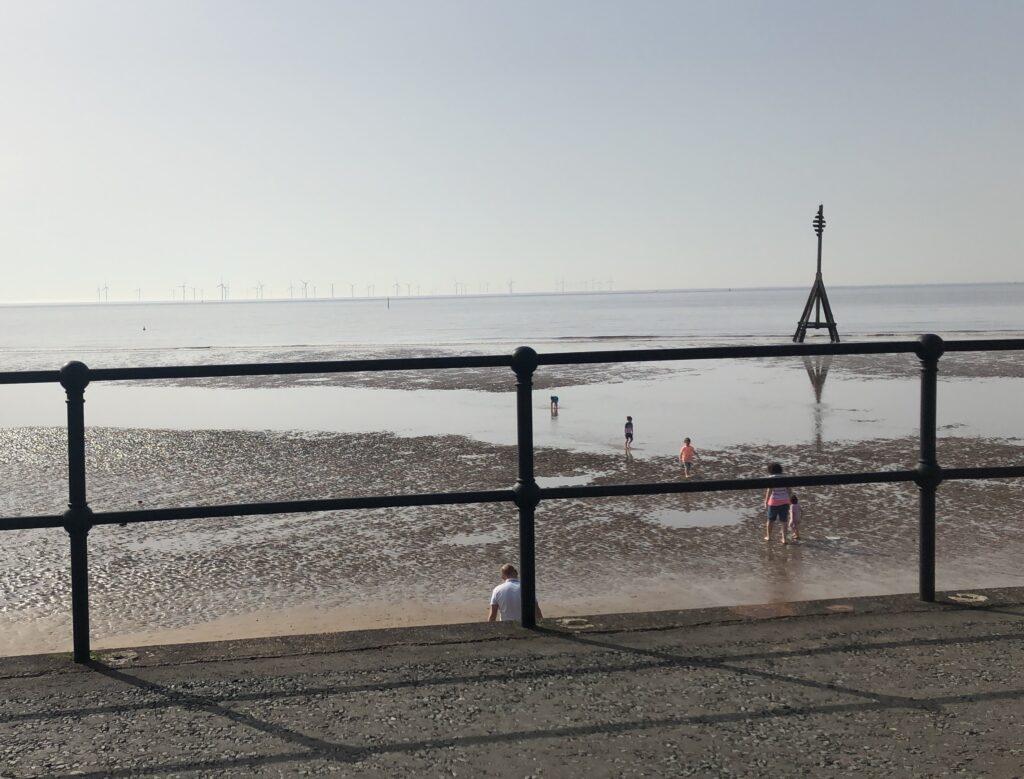 Photo of a beach with grey sky, children and railings