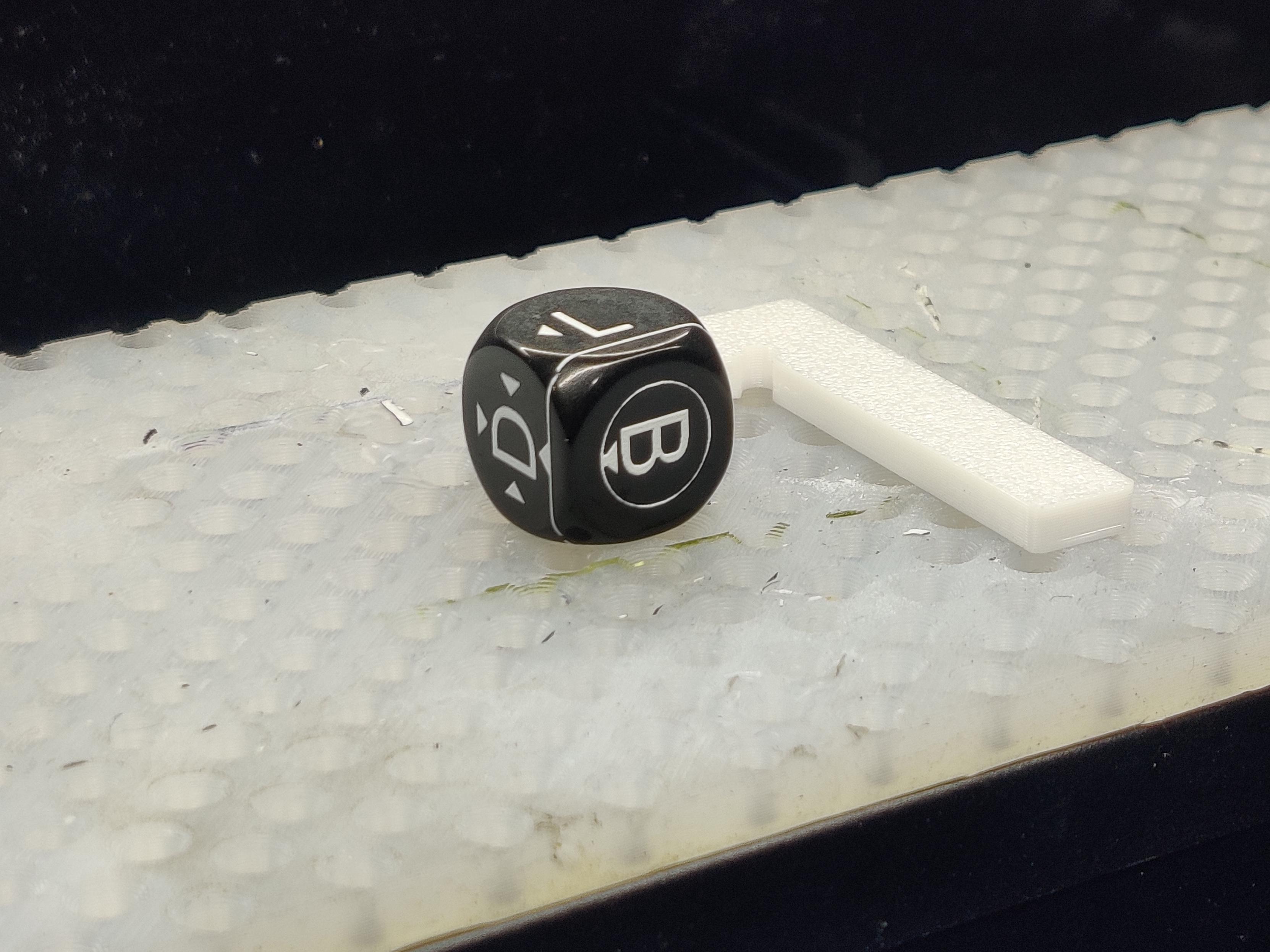 A black acrylic cube with white letters, arrows, lines and circles, on a silicone bed
