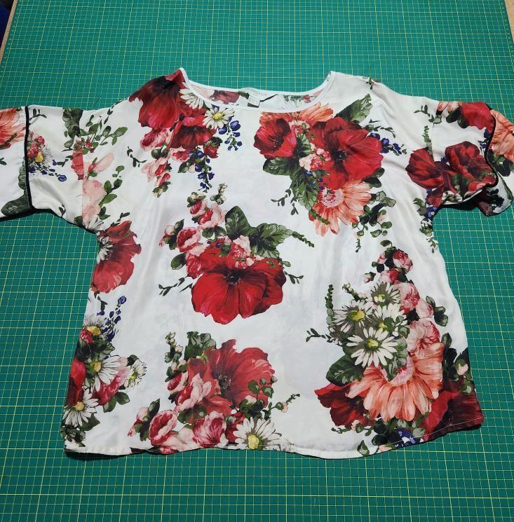 A rose-patterned white silk t shirt on a green cutting board