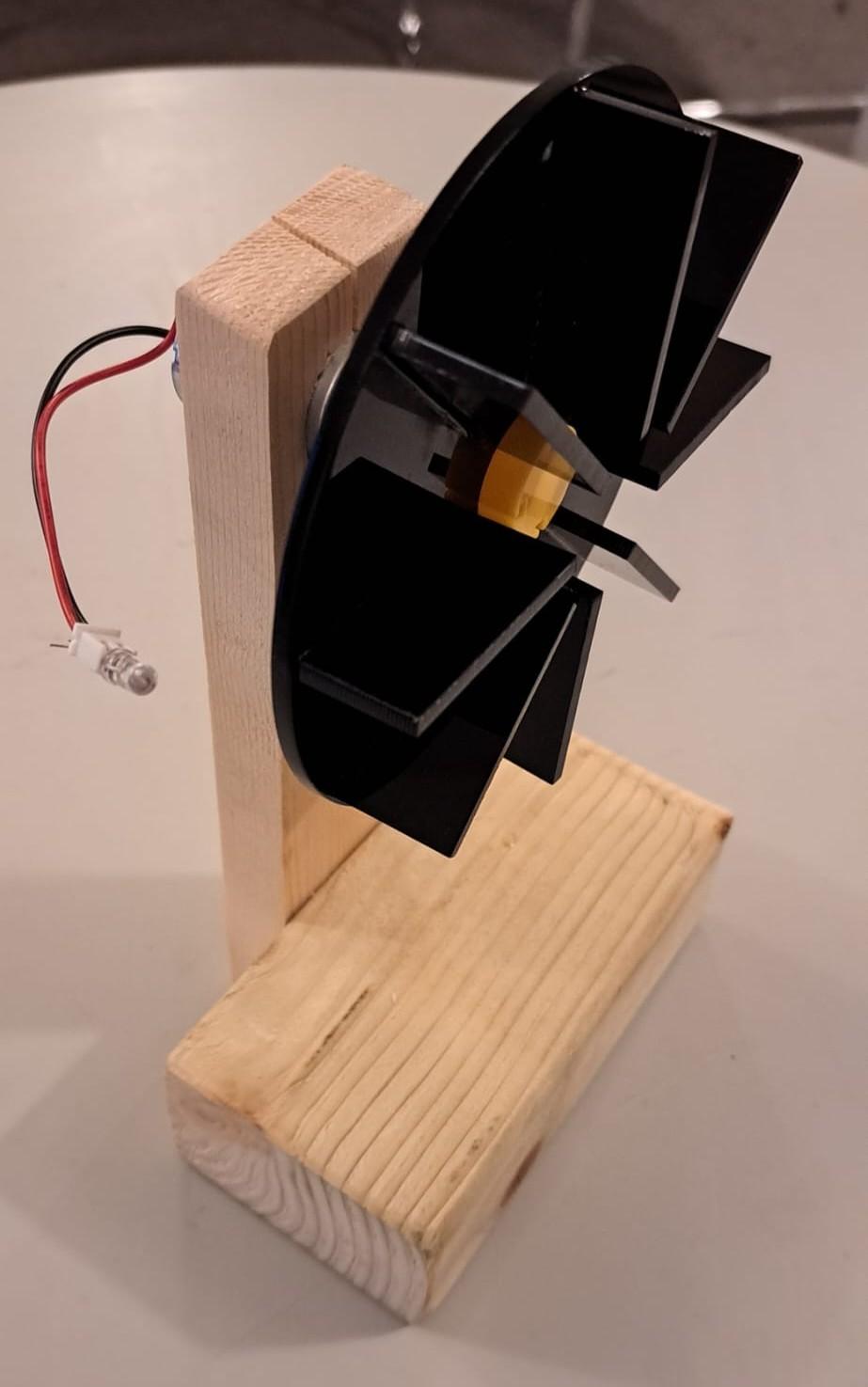 A black acrylic fan attached to a wooden support, with electrical leads