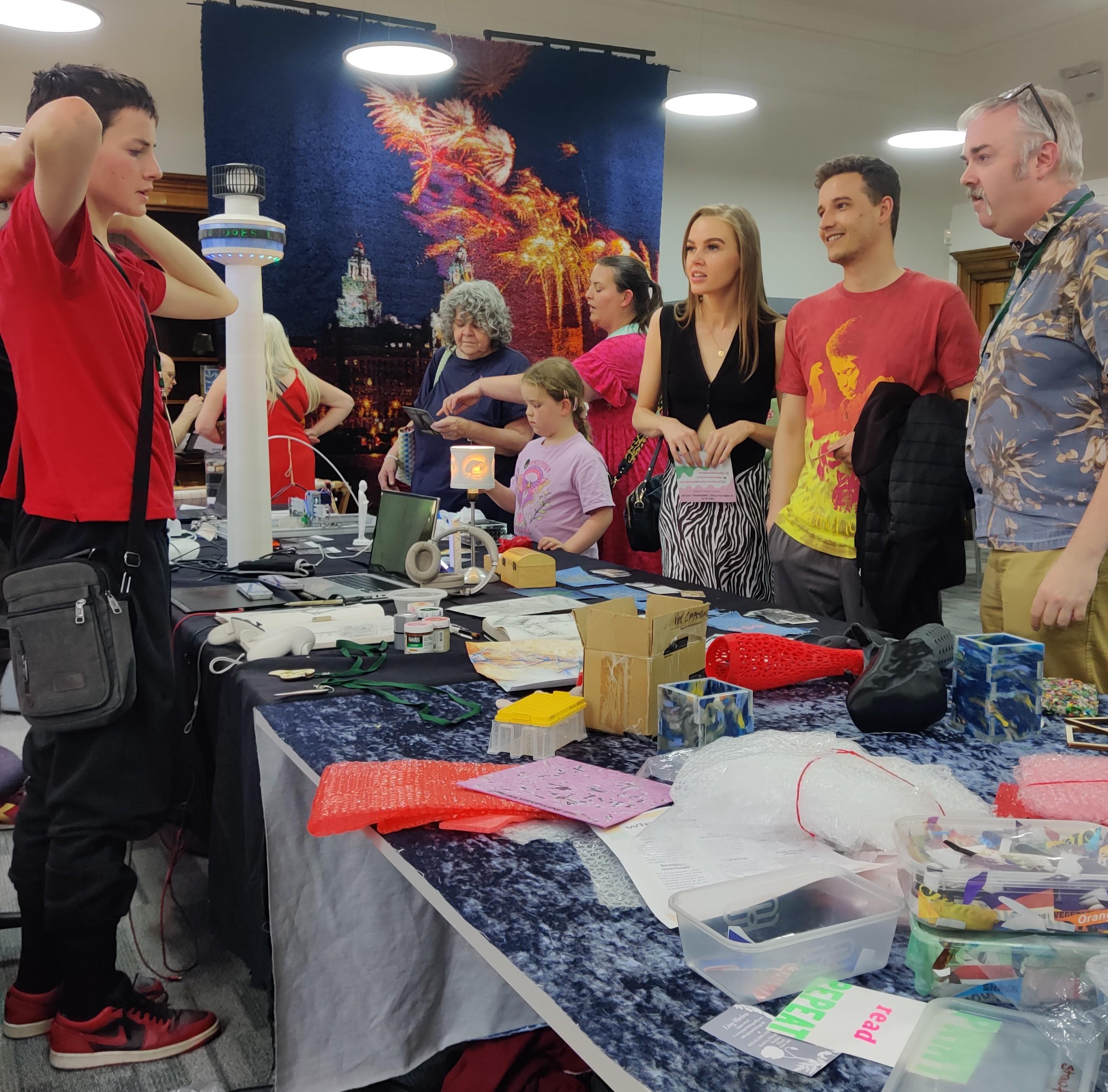 DoES Liverpool people and visitors standing round tables with 3d printed models and bubble wrap sheets.