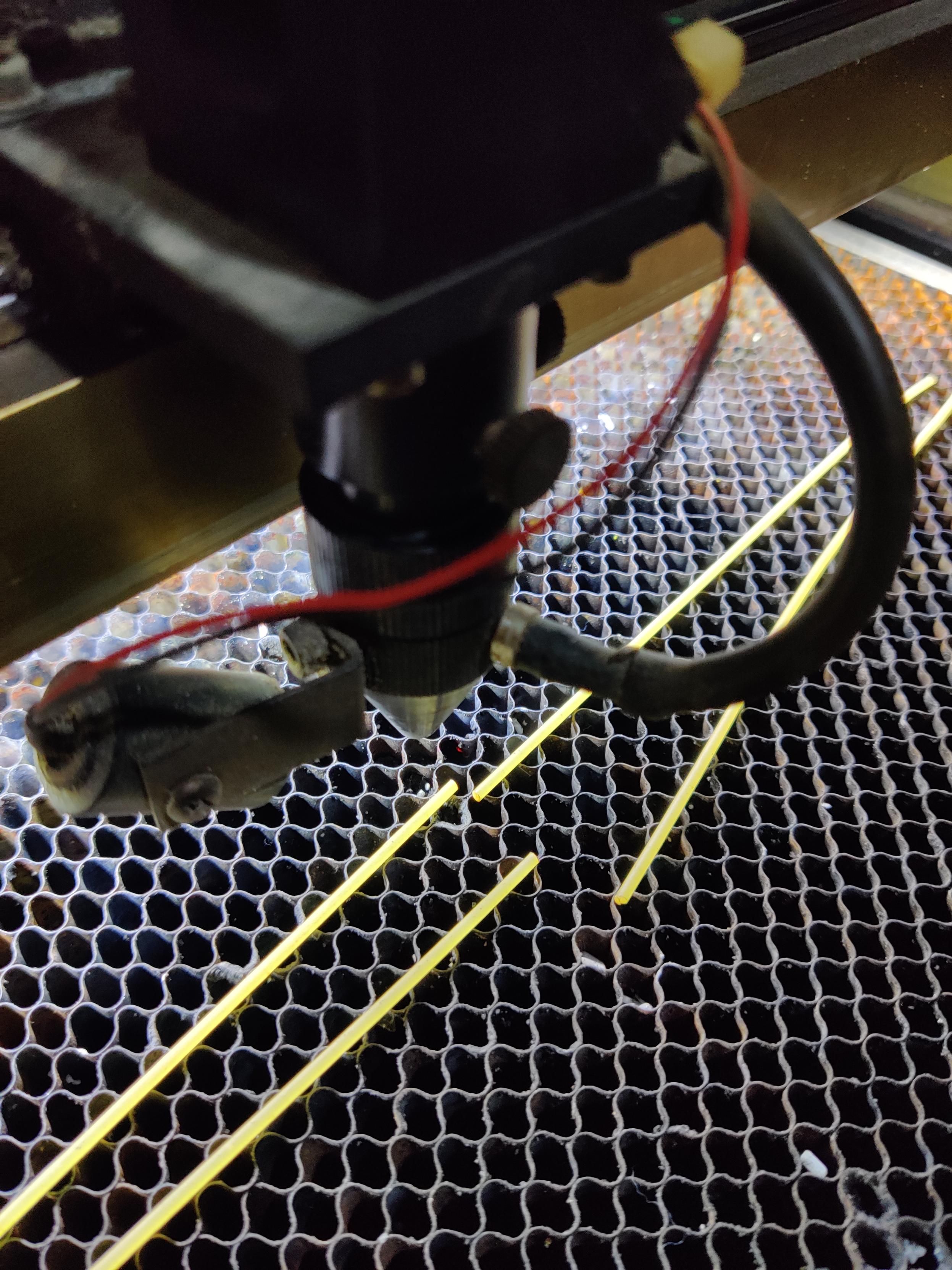 Two pieces of spaghetti that have been cut in two, on a laser cutter bed