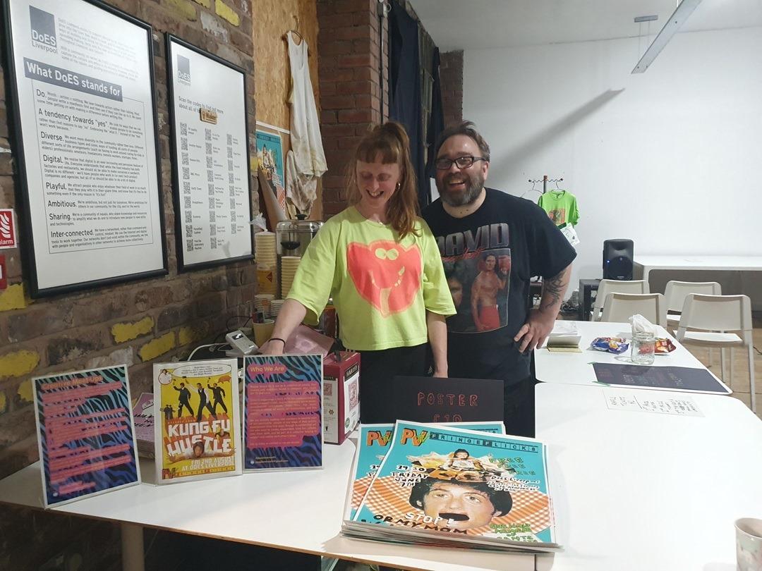 Ronda and Simon standing behind a white table with posters