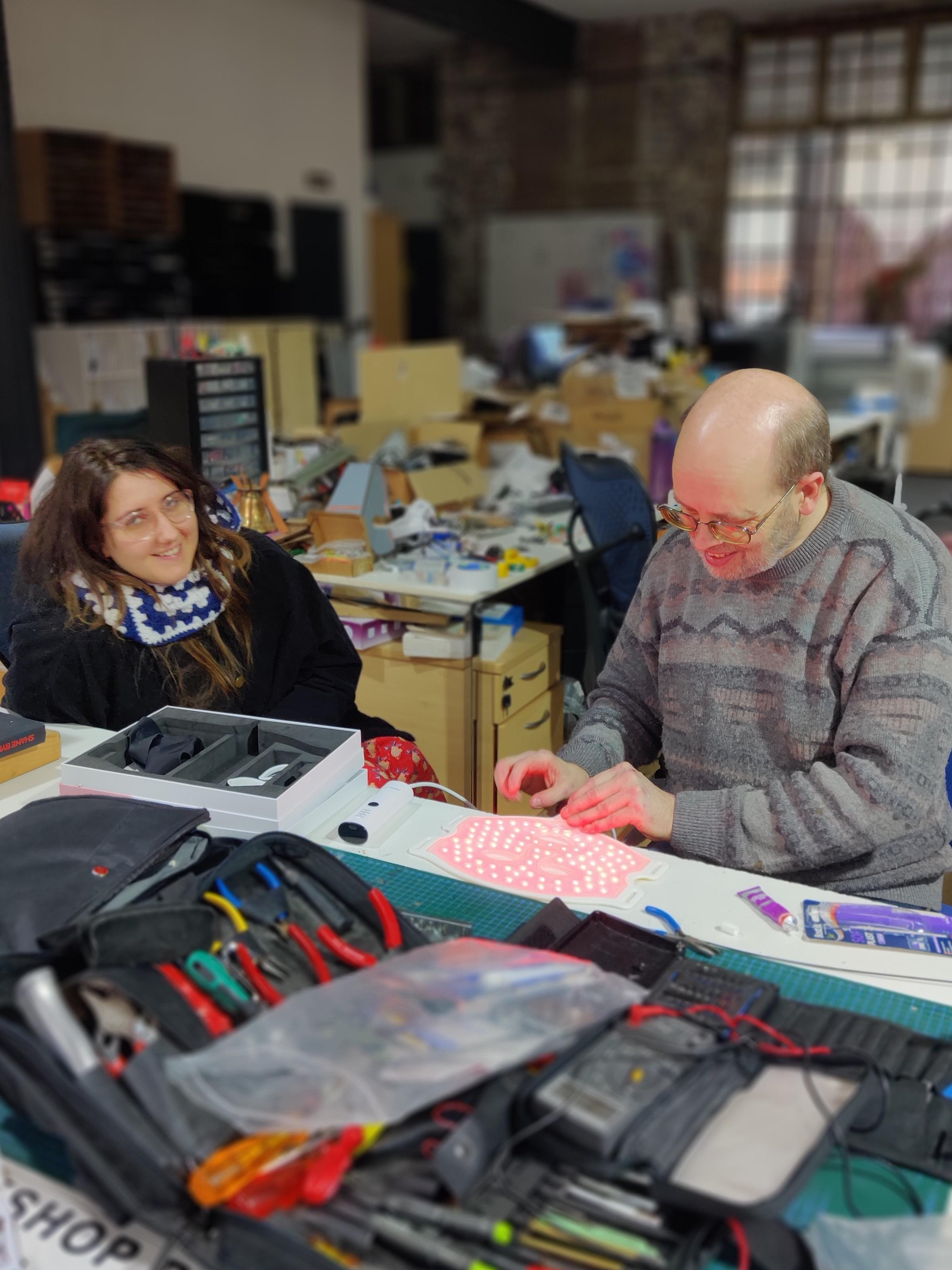 Mike G fixing LEDs on a facemask while the owner looks on