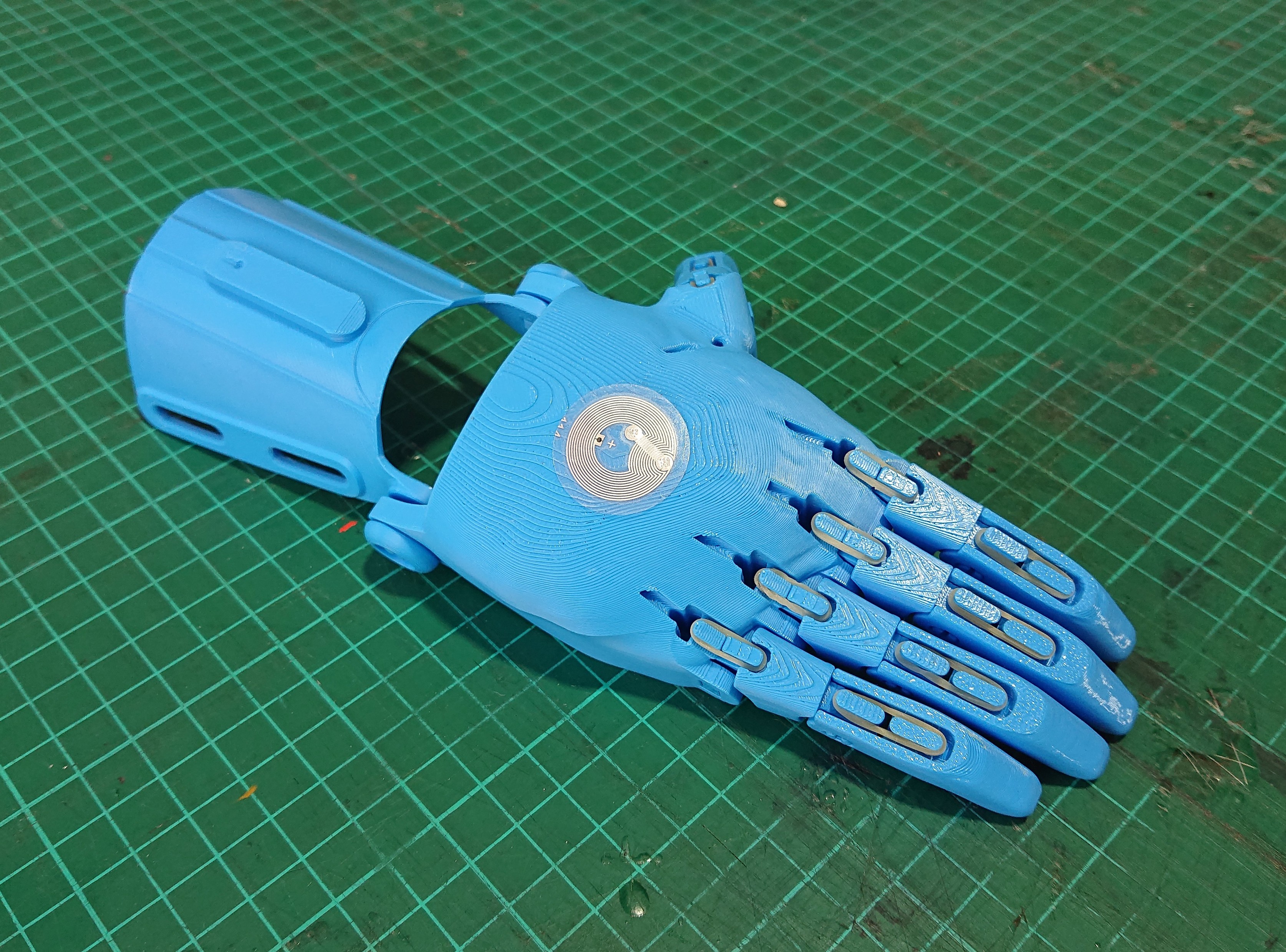 A 3D print of an E-nabling the Future open-source prosthetic hand, printed in blue plastic. The small metal NFC sticker for Museum in a Box to recognise can be seen on the back of the hand.