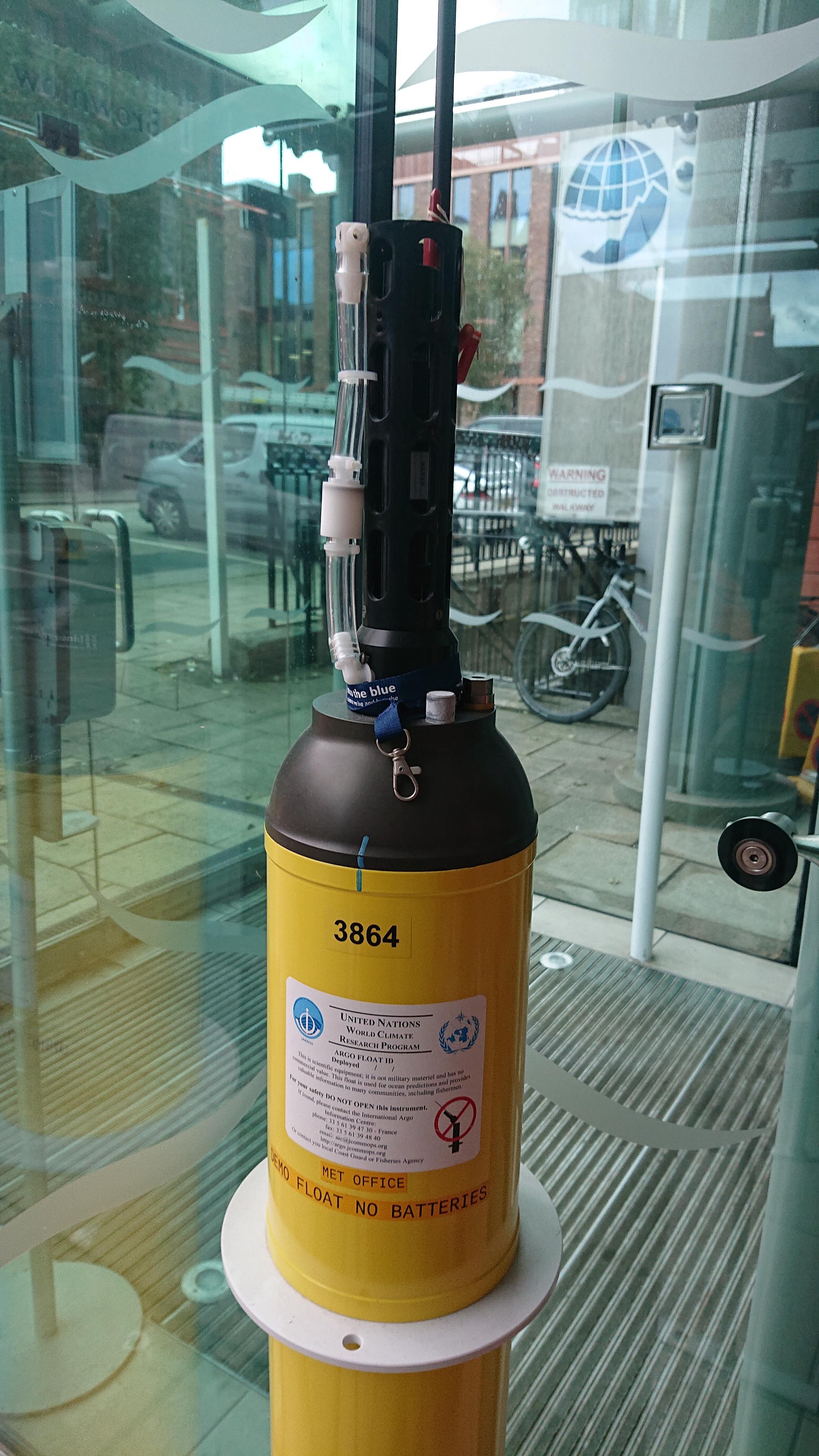 A tall thin metal cylinder, painted yellow, with a protrusion of sensors poking out of the top