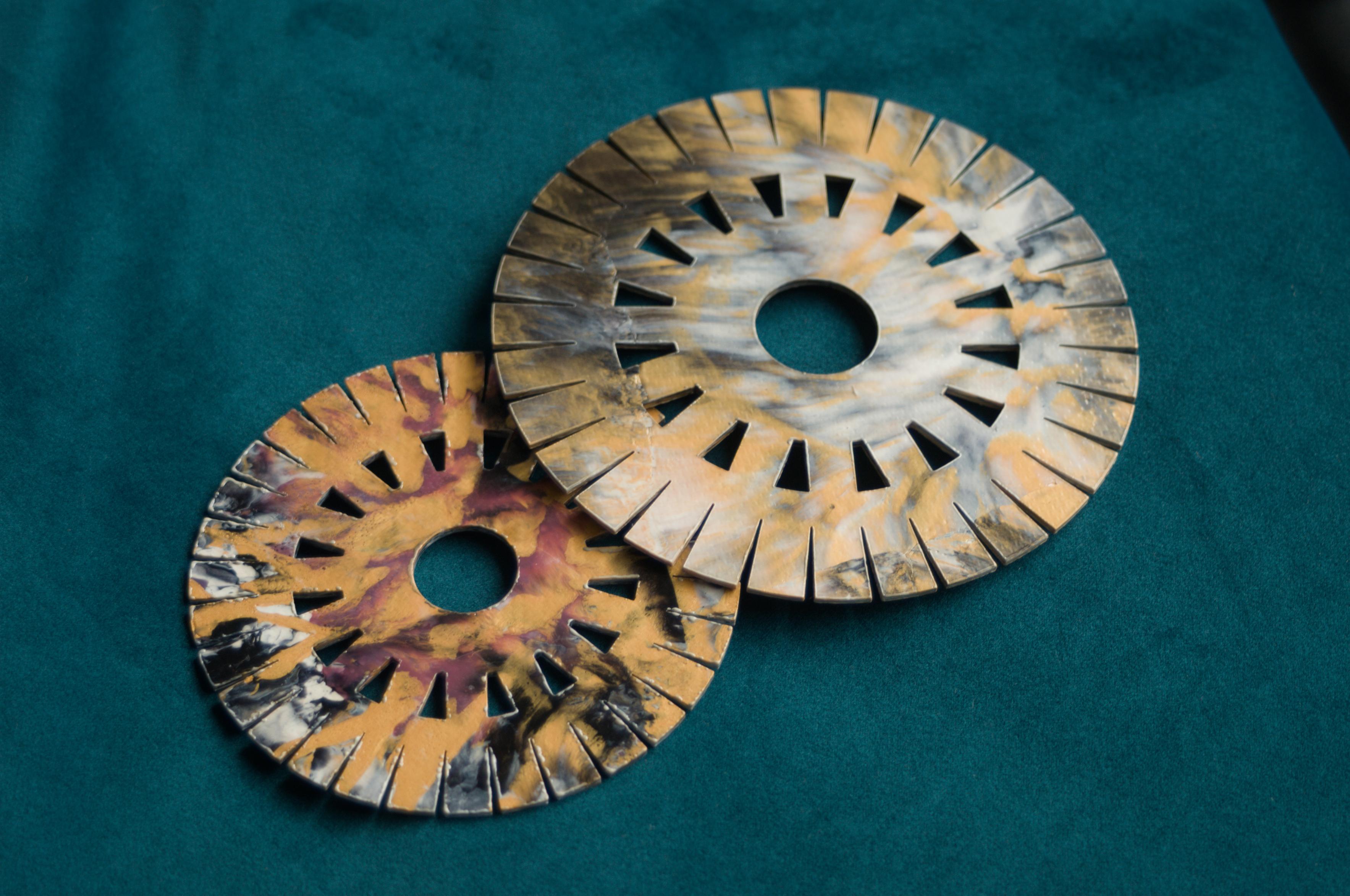 Two different-sized, finished kumihimo discs overlapping one another on a teal background.