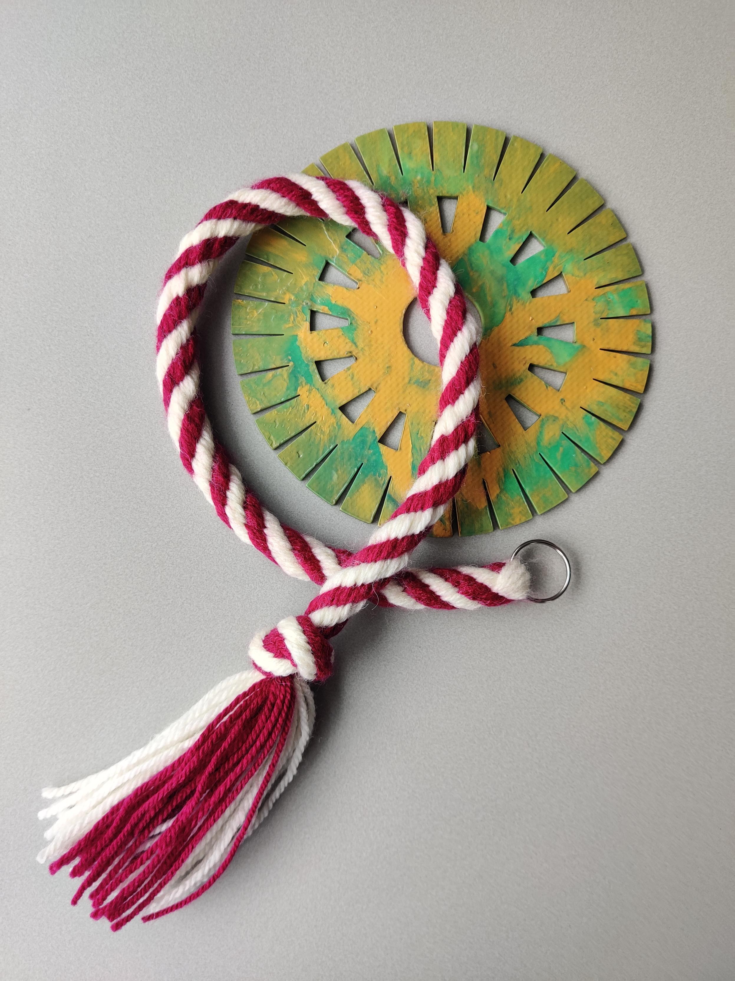 A long red and white striped 16 element Kongo Gumi braid lying on a large mottled green and gold kumihimo disk