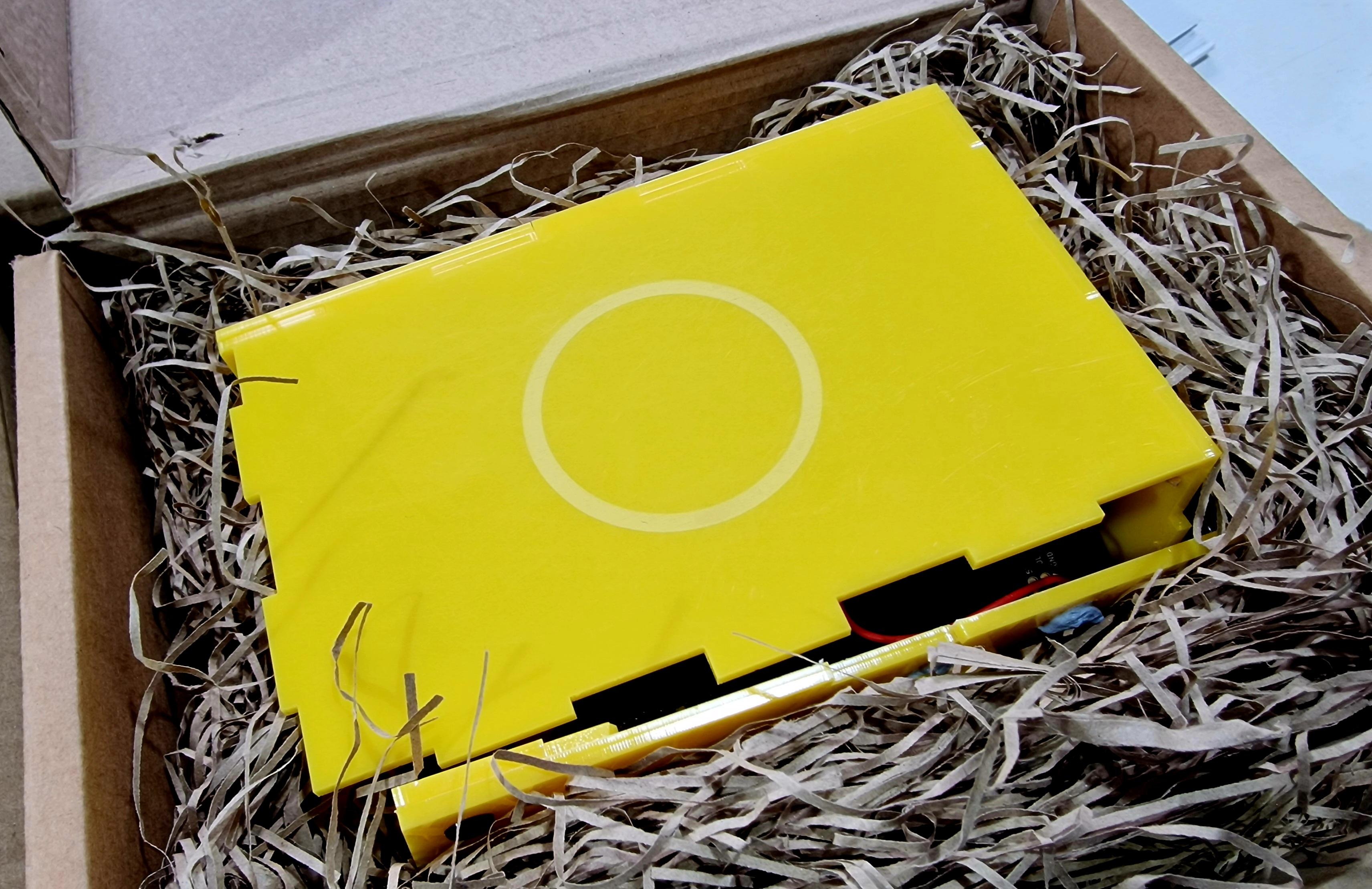 A yellow acrylic museum in a box packed in a lot of shredded paper in a cardboard box. This one is in for repair after being involved in a nasty smash. It will be fixed and heading back to its library today.