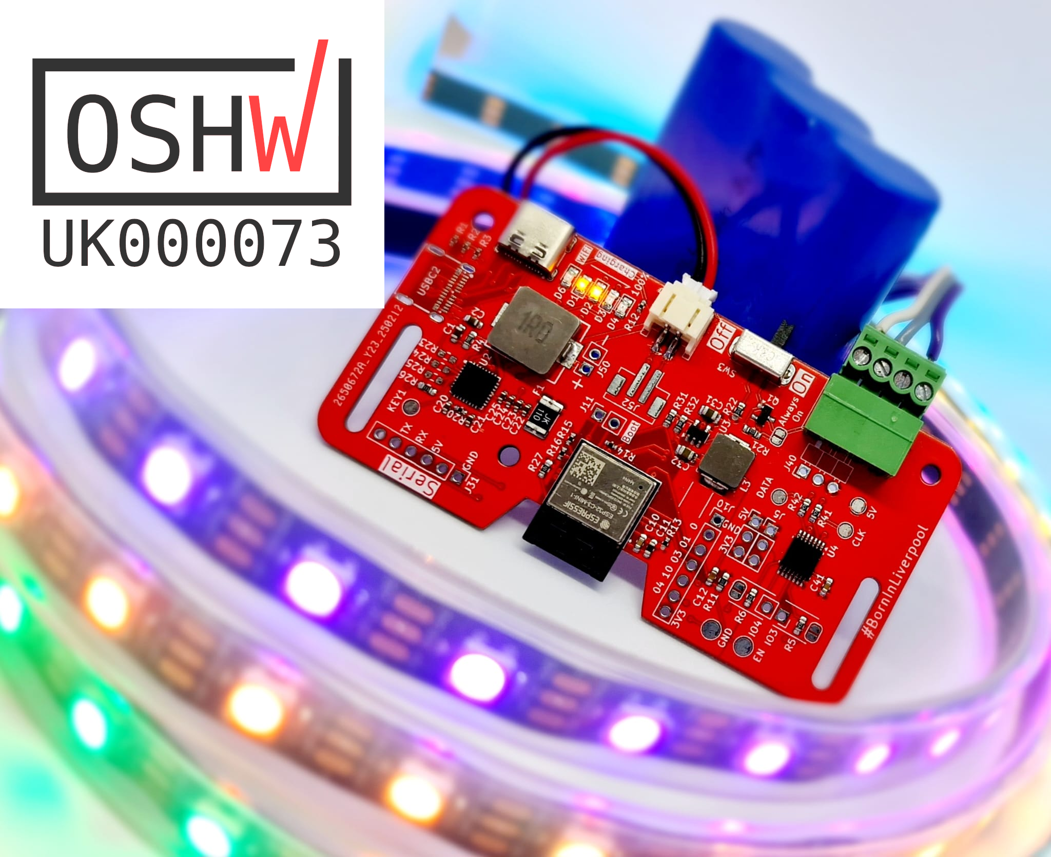 Red circuit board with a blue battery in the background. In the foreground is a string of multicoloured leds In the top left corner is the OSHWA registration number UK00073