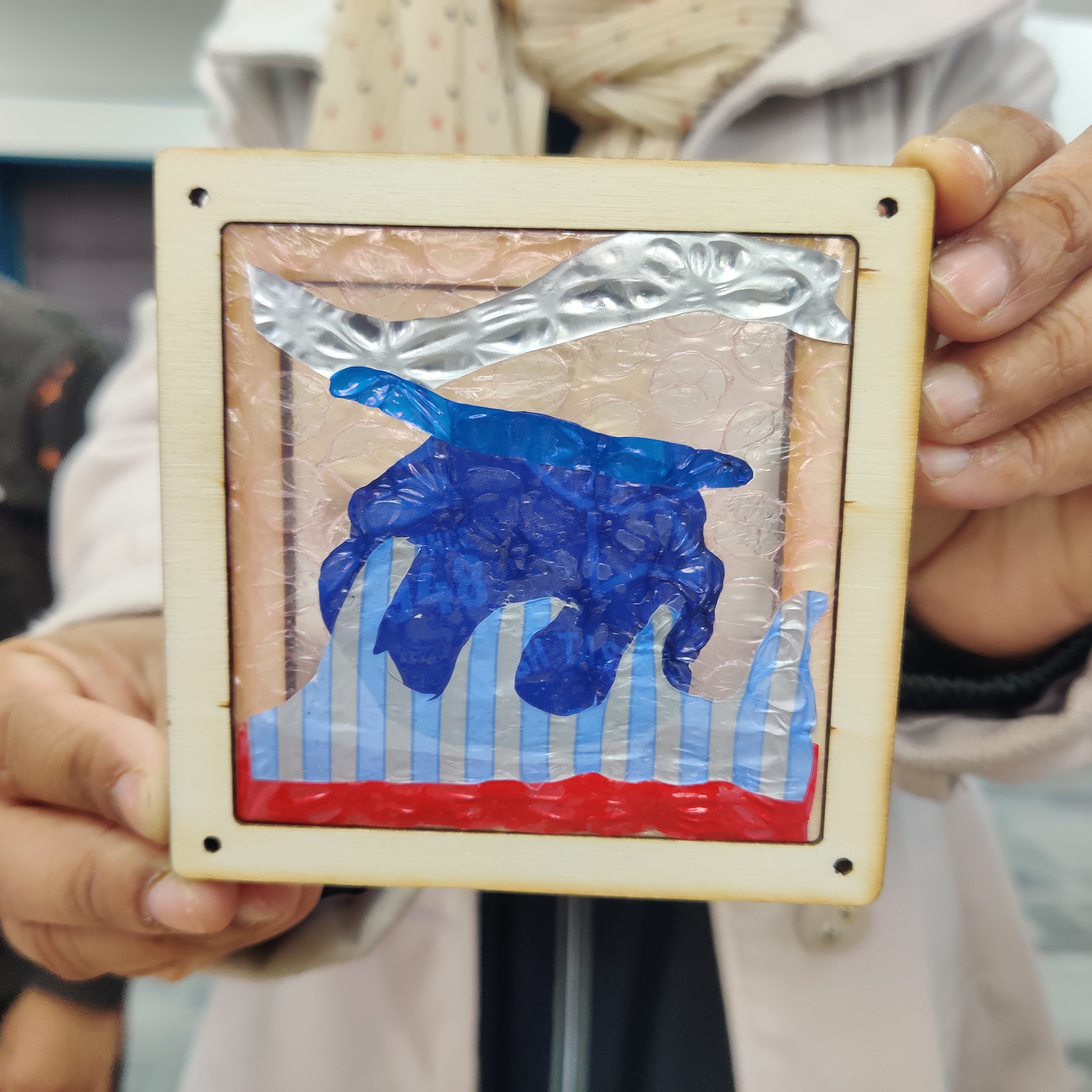 Hands holding up an ironed soft plastic picture in a laser cut ply frame.