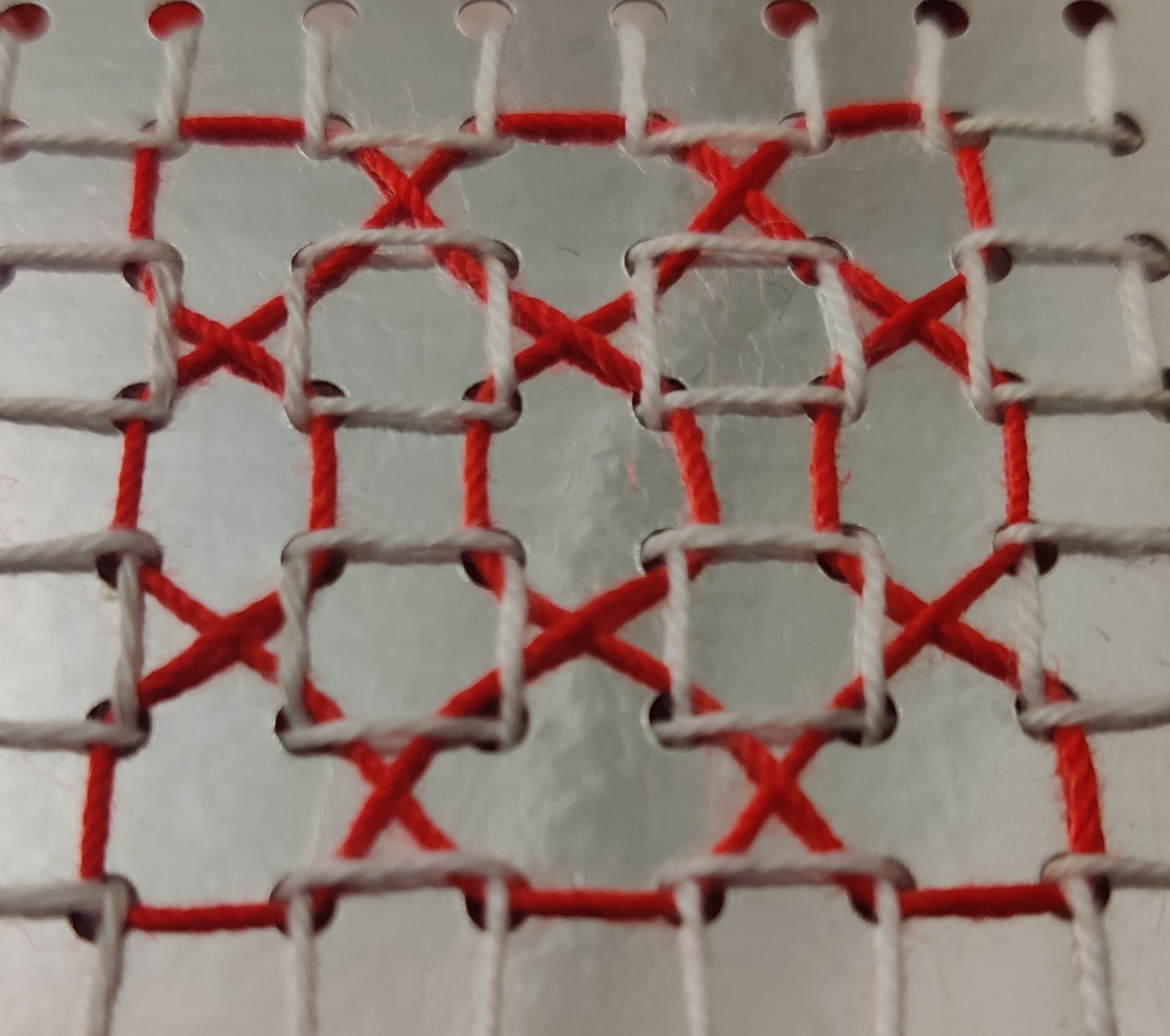 Red thread woven in and out of a white thread grid on silver card