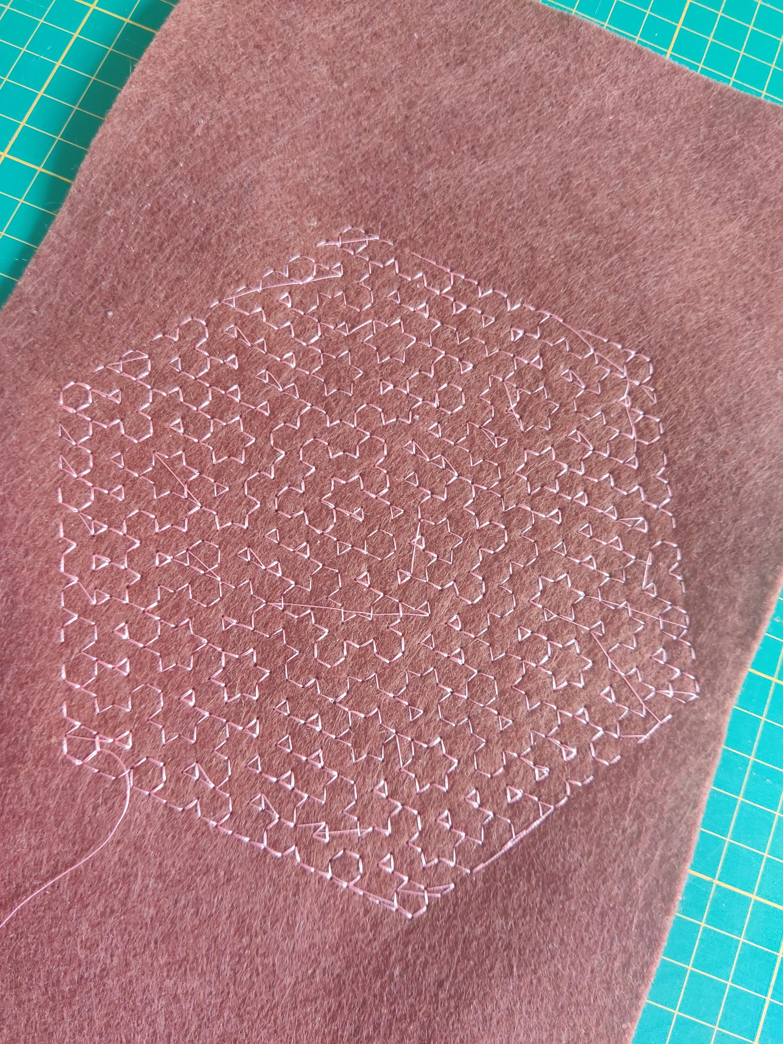 Unfinished machine embroidered Hitomezashi in light thread on a brown felt background