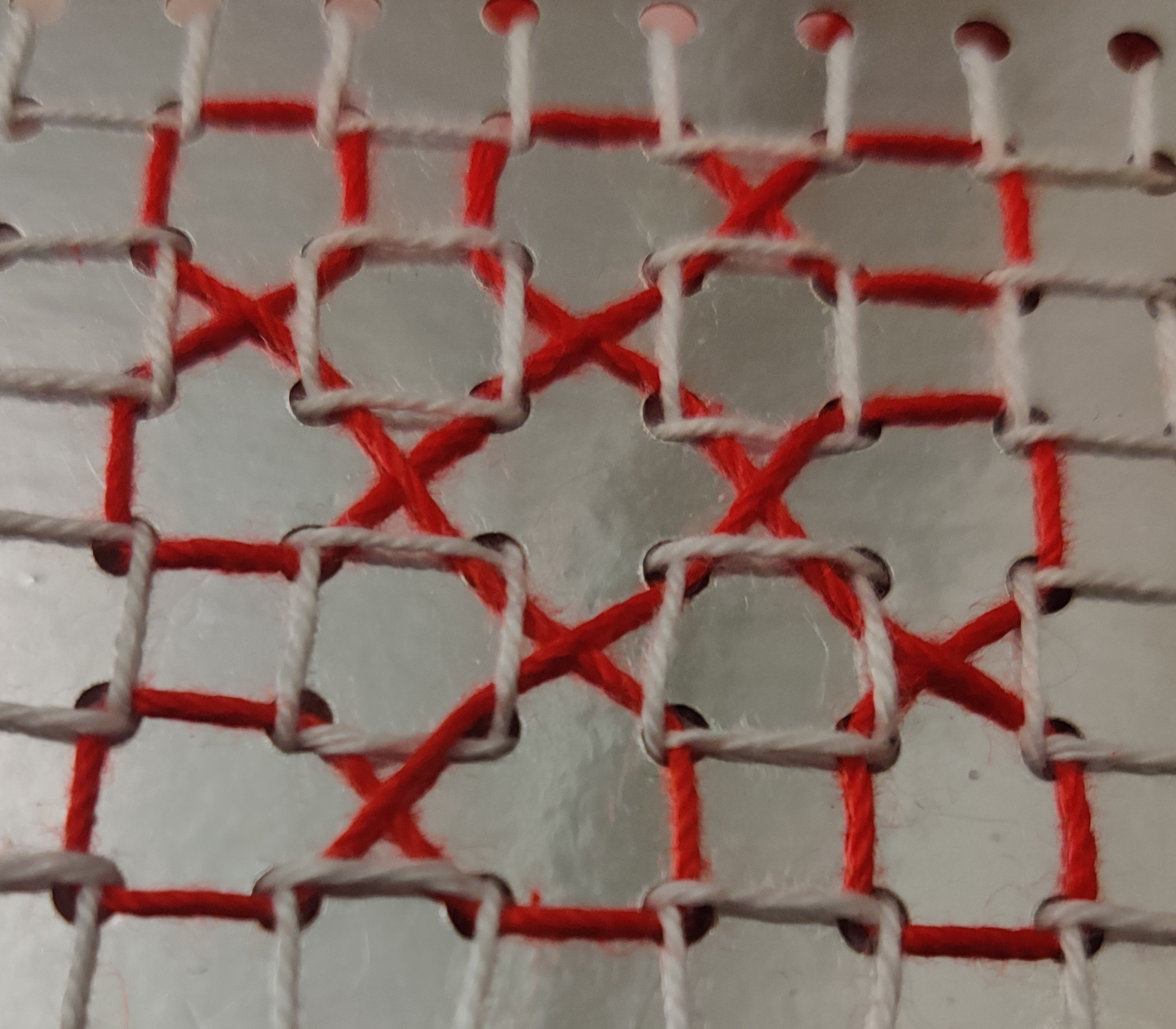 Red thread woven in and out of a white thread grid on silver card