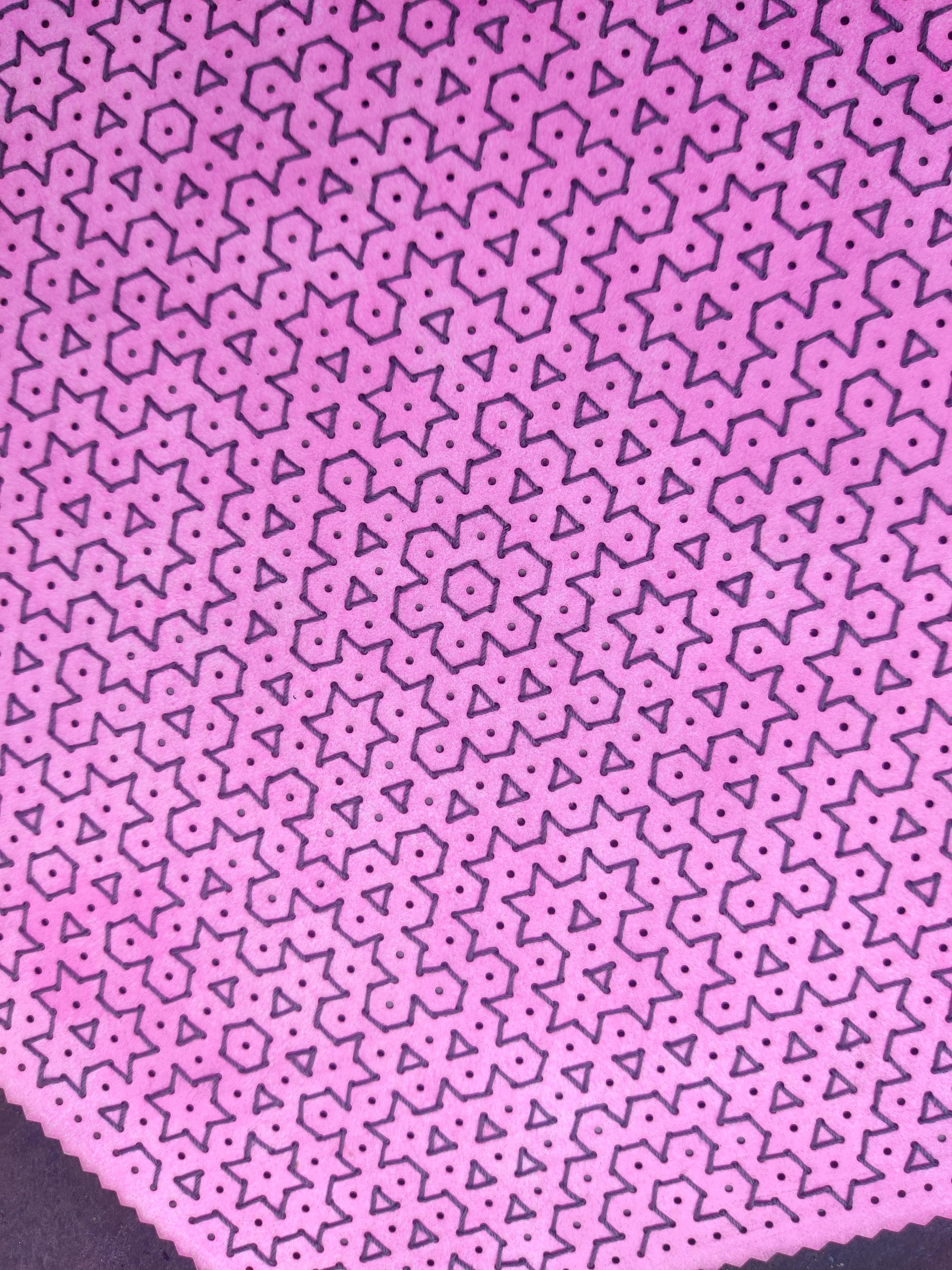Close up of Hitomezashi embroidery in dark grey crochet cotton on a hexagonal piece of card which has been unevenly coloured with a pink stamp and laser cut with an isometric dot grid and zigzag edges