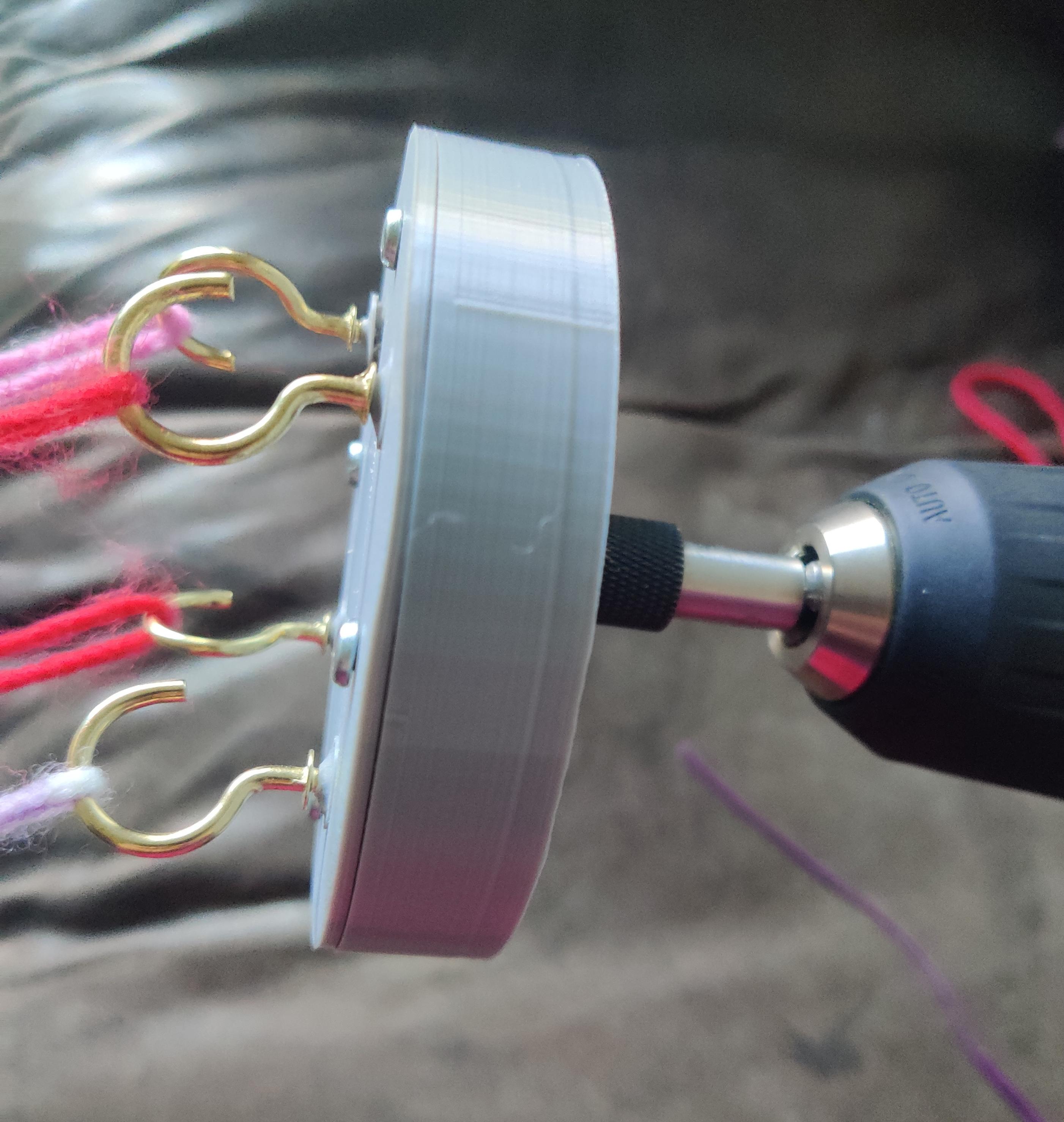 Grey 3d printed drill attachment with gold coloured hooks, attached to drill