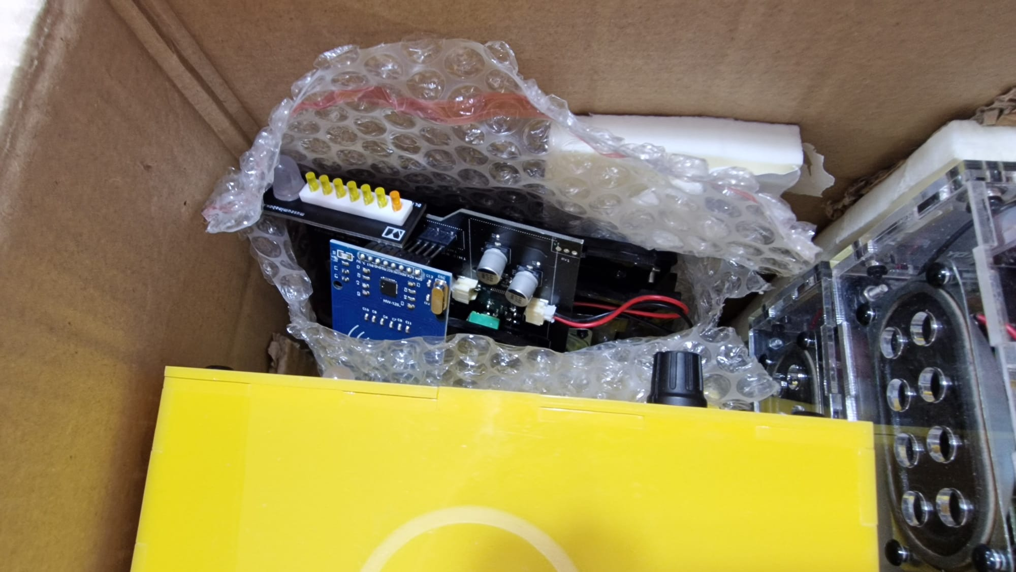 A close up of one corner of the cardboard box, showing the edges of the clear and yellow boxes and, wrapped in bubble-wrap, the constituent parts of another box - looking rather like it's been supplied as a 