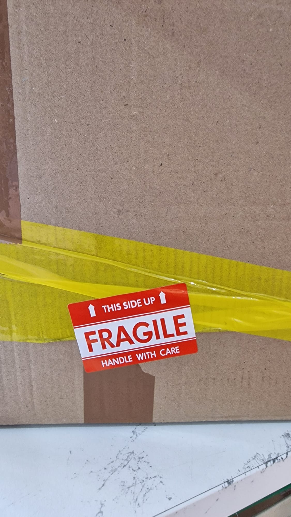 A cardboard box with some yellow tape across it and a red-and-white sticker on it reading 