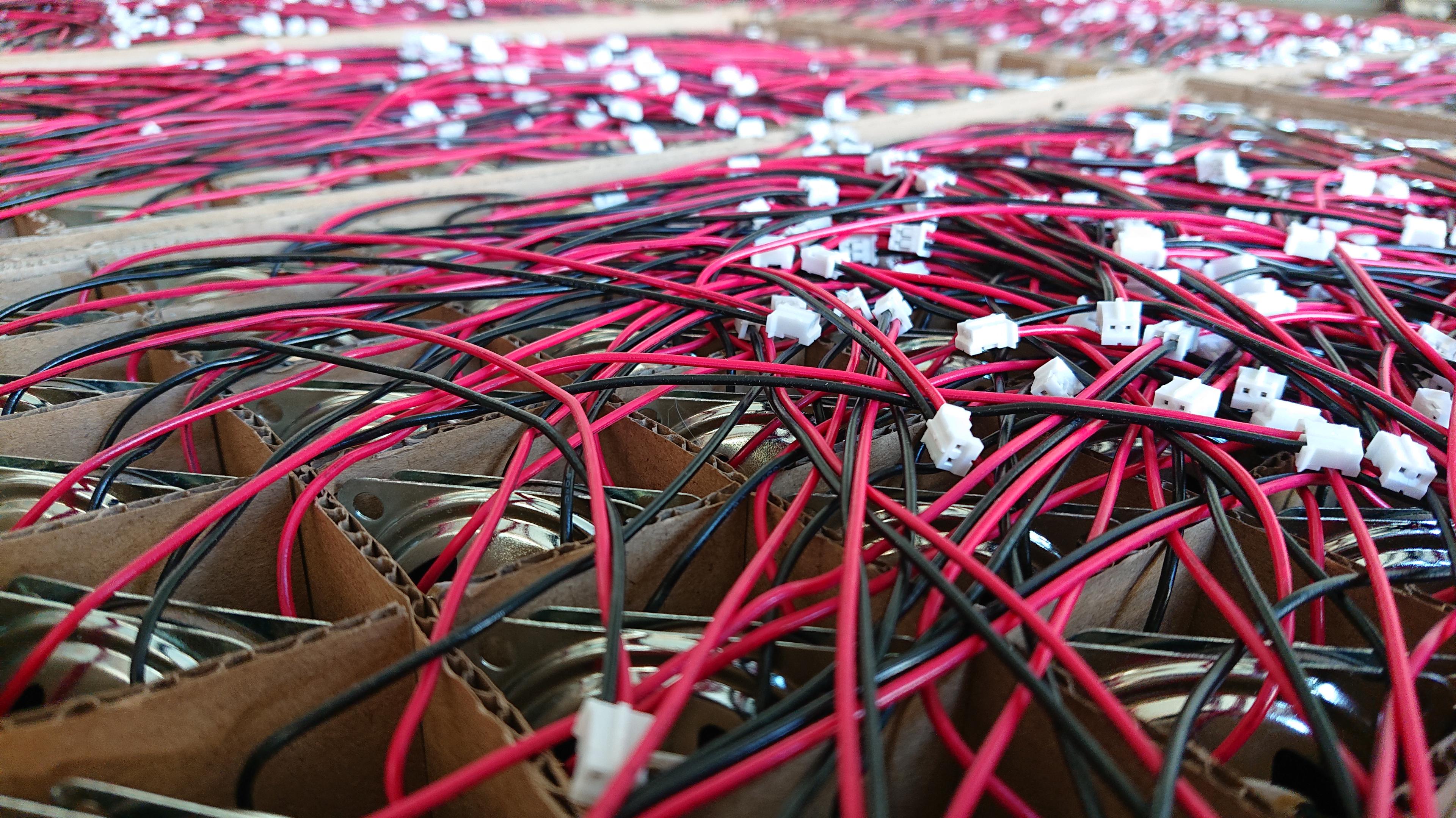 Looking out across a sea of speakers, all slotted in pairs into a grid of gaps in the cardboard packaging. Not that it's too easy to spot that they're speakers, the silver of the frame is just about visible in the ones nearest to us, and mostly it looks like a massed tangle of red and black wires dotted with white JST connectors