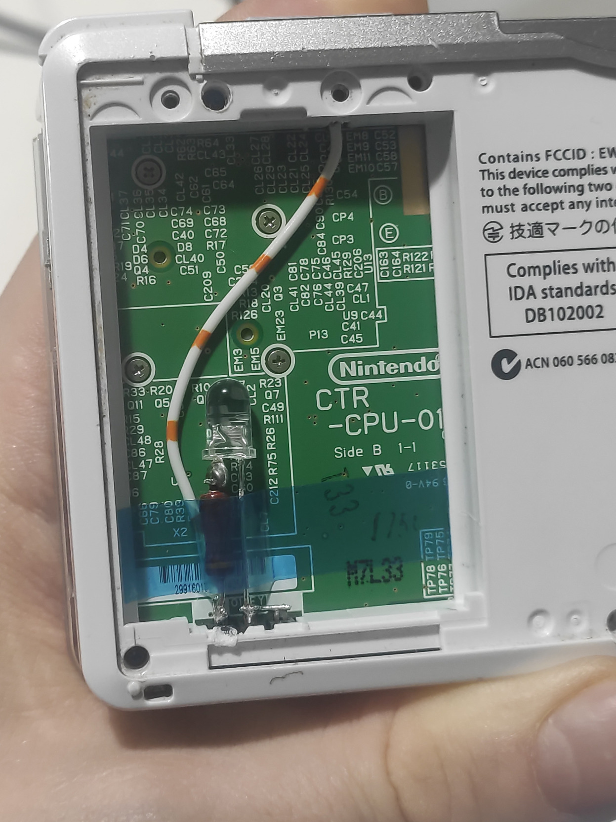 The back of a 3DS with its backplate removed and battery taken out. The silk screen of the 3DS is visible and bears the Nintendo logo. Our bodge wire and LED is proudly shown.