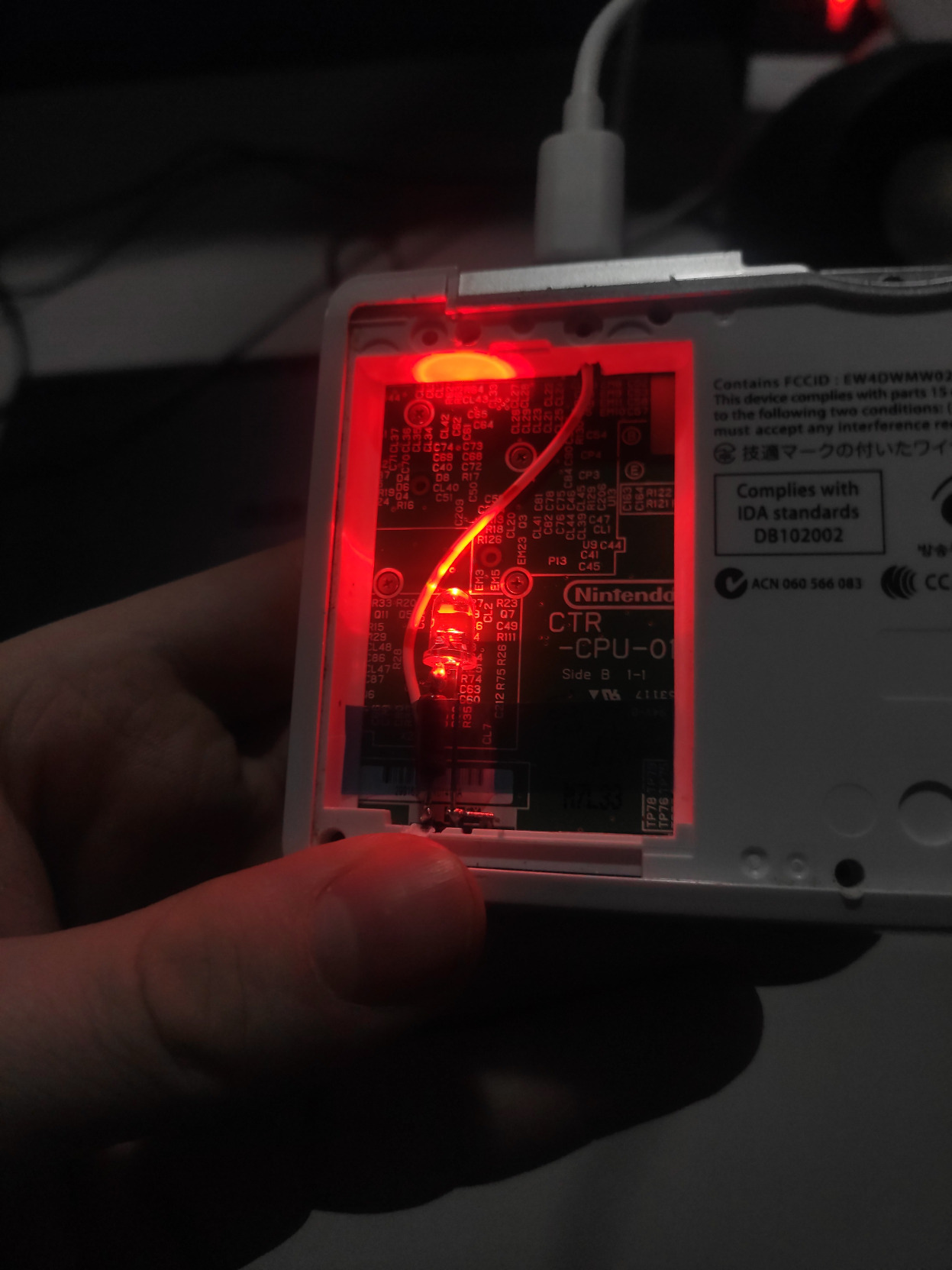 A closeup picture of the 3DS back with silkscreen exposed and red LED from our bodge turned on.